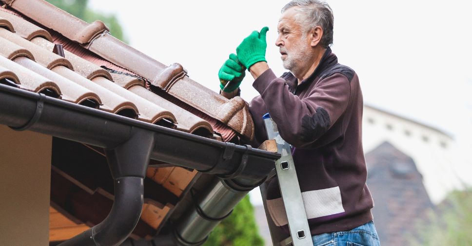 Homem tentando instalar calhas sozinho. Saiba mais!